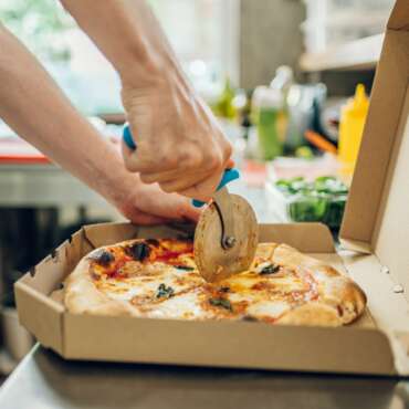 Hand of kitchen chef cutting pizza with a pizza cutter